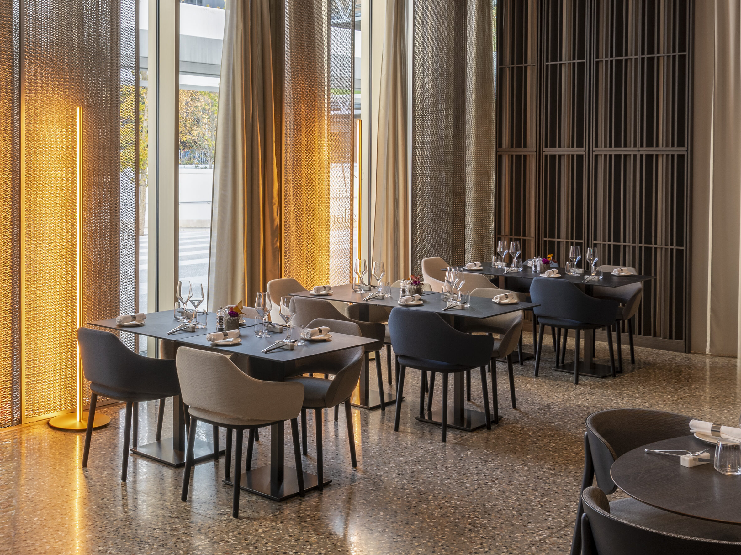 Restaurant d’hôtel lumineux, tables dressées devant de grandes baies vitrées