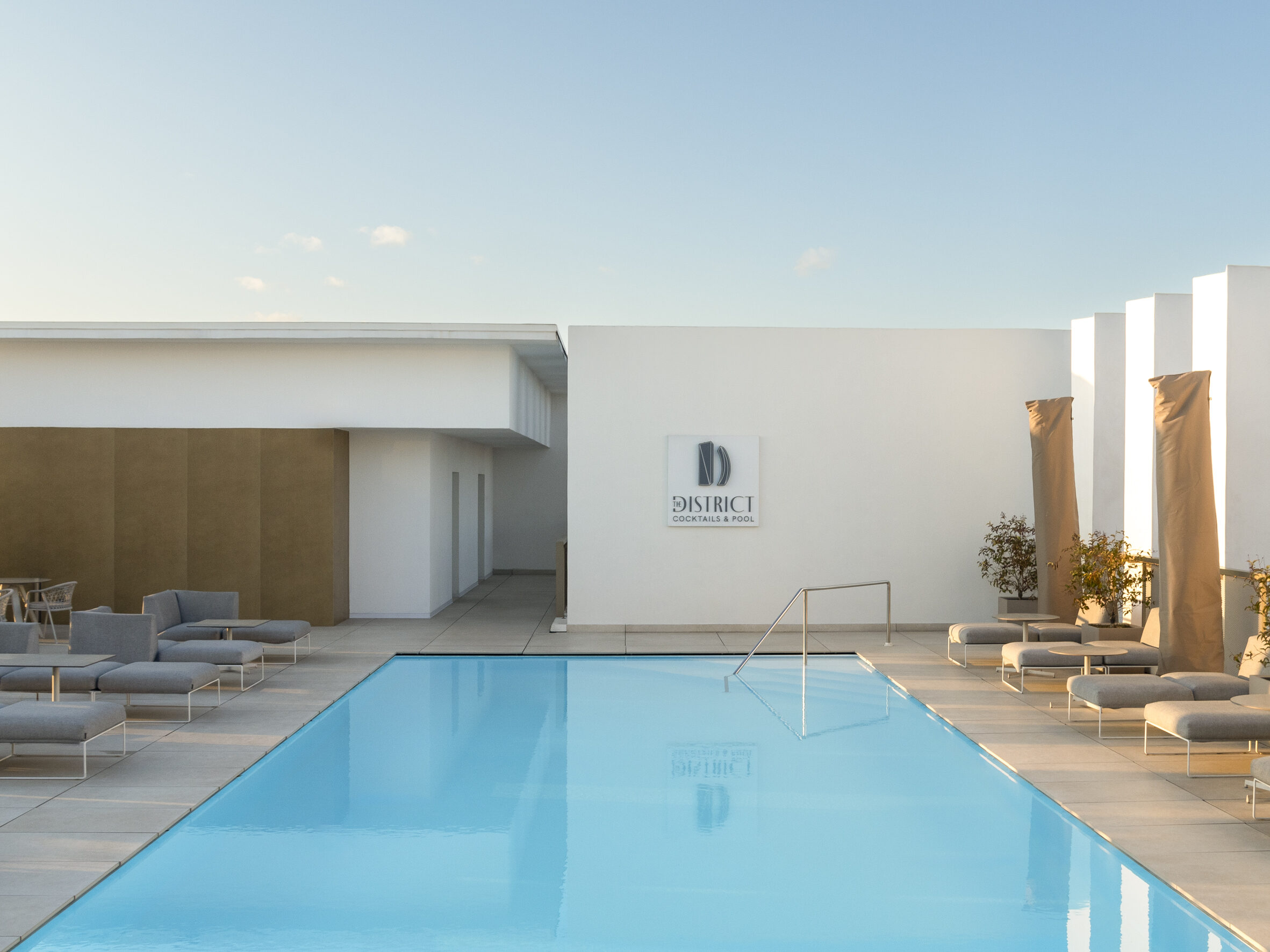 Piscine sur le toit d’un hôtel, transats et murs blancs dans la lumière du soir