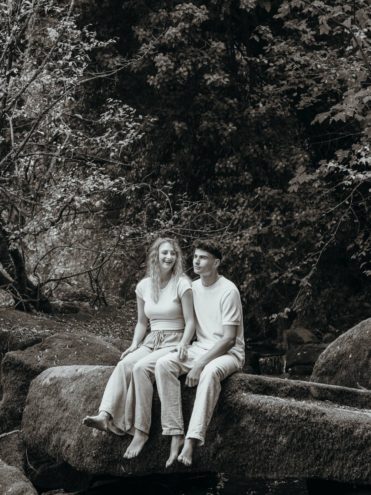 Couple assis en riant sur un grand rocher en forêt, noir et blanc