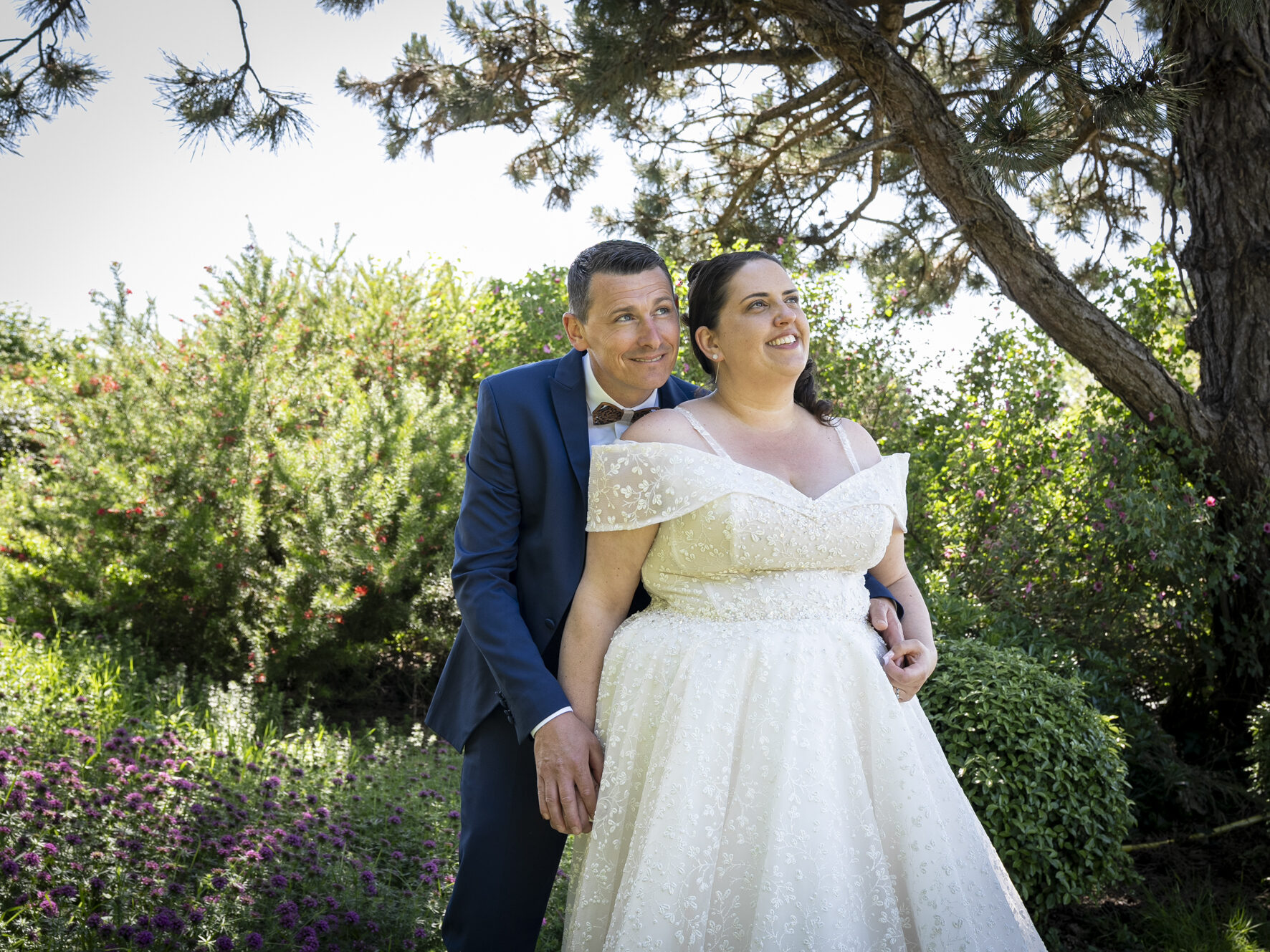 Marié enlaçant la mariée dans un jardin fleuri, par une journée ensoleillée