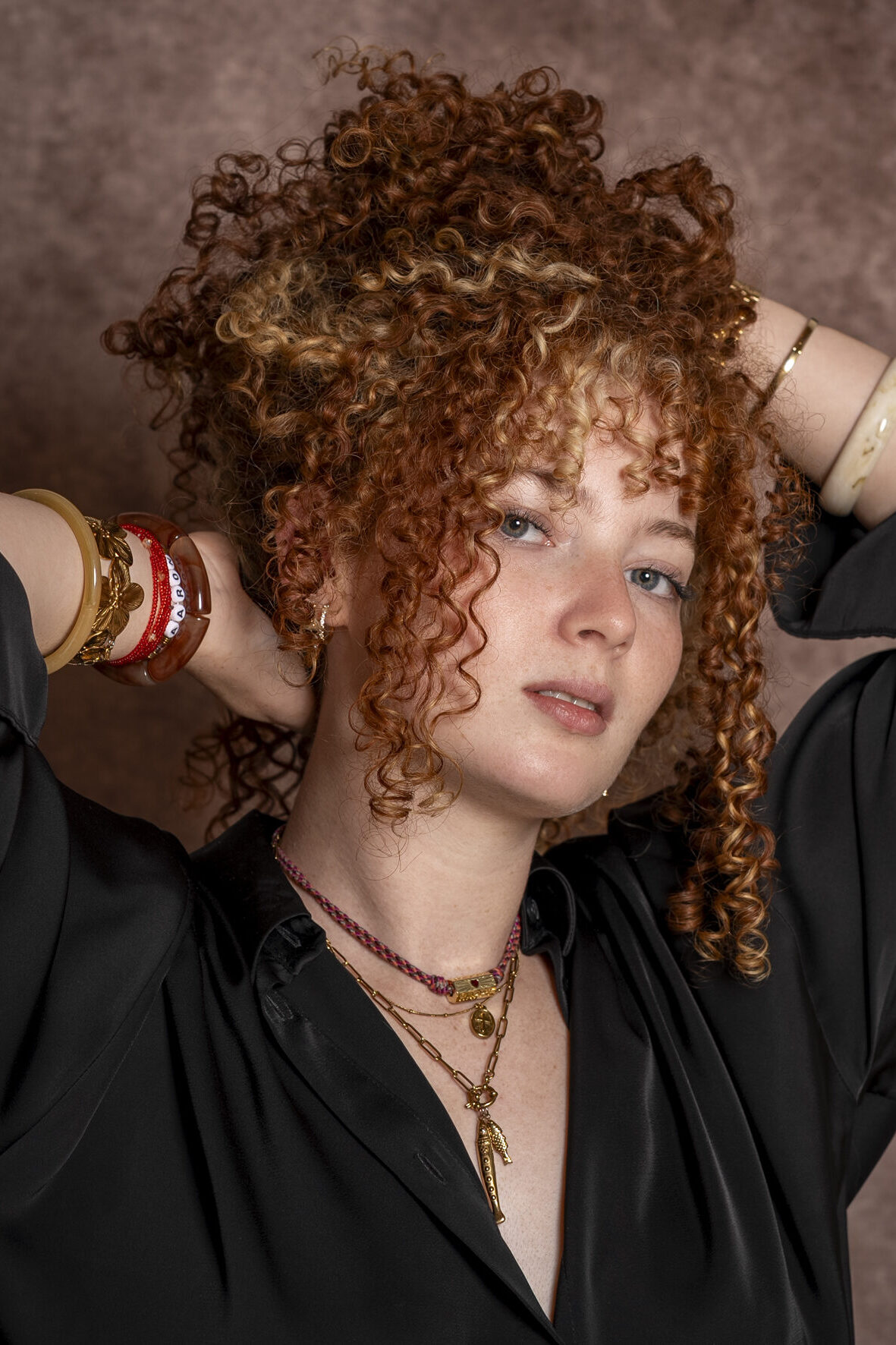 Portrait studio d’une jeune femme aux cheveux roux bouclés, chemise noire et bracelets