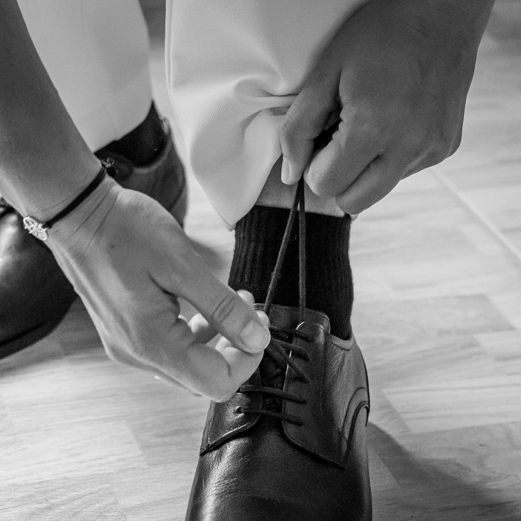 Mains laçant une chaussure de cuir noir pendant les préparatifs, noir et blanc