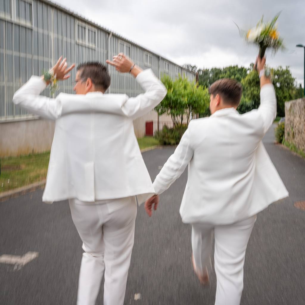 Les mariées de dos, bras levés de joie, bouquet lancé vers le ciel