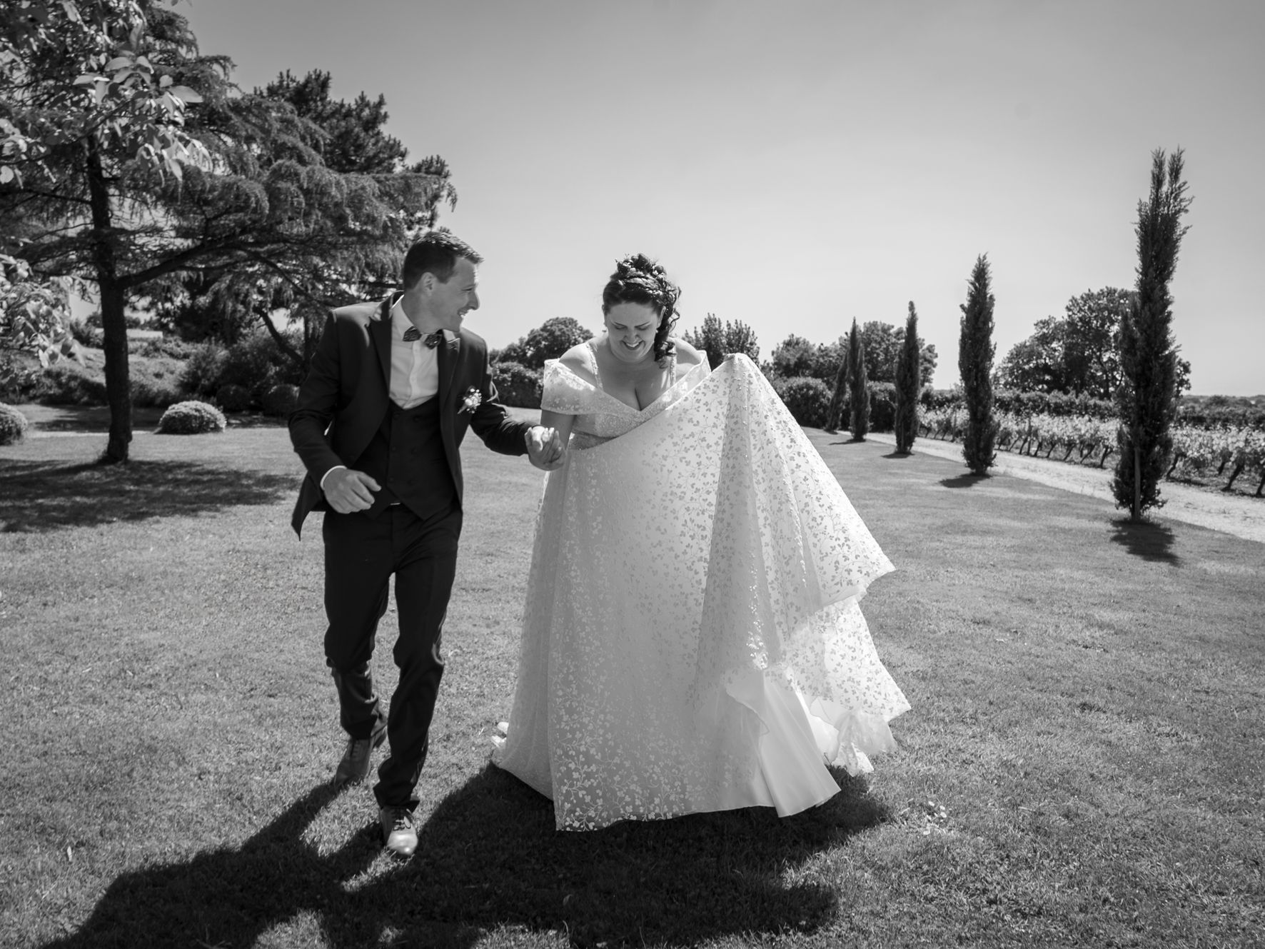 Mariés courant main dans la main dans un parc bordé de vignes, noir et blanc