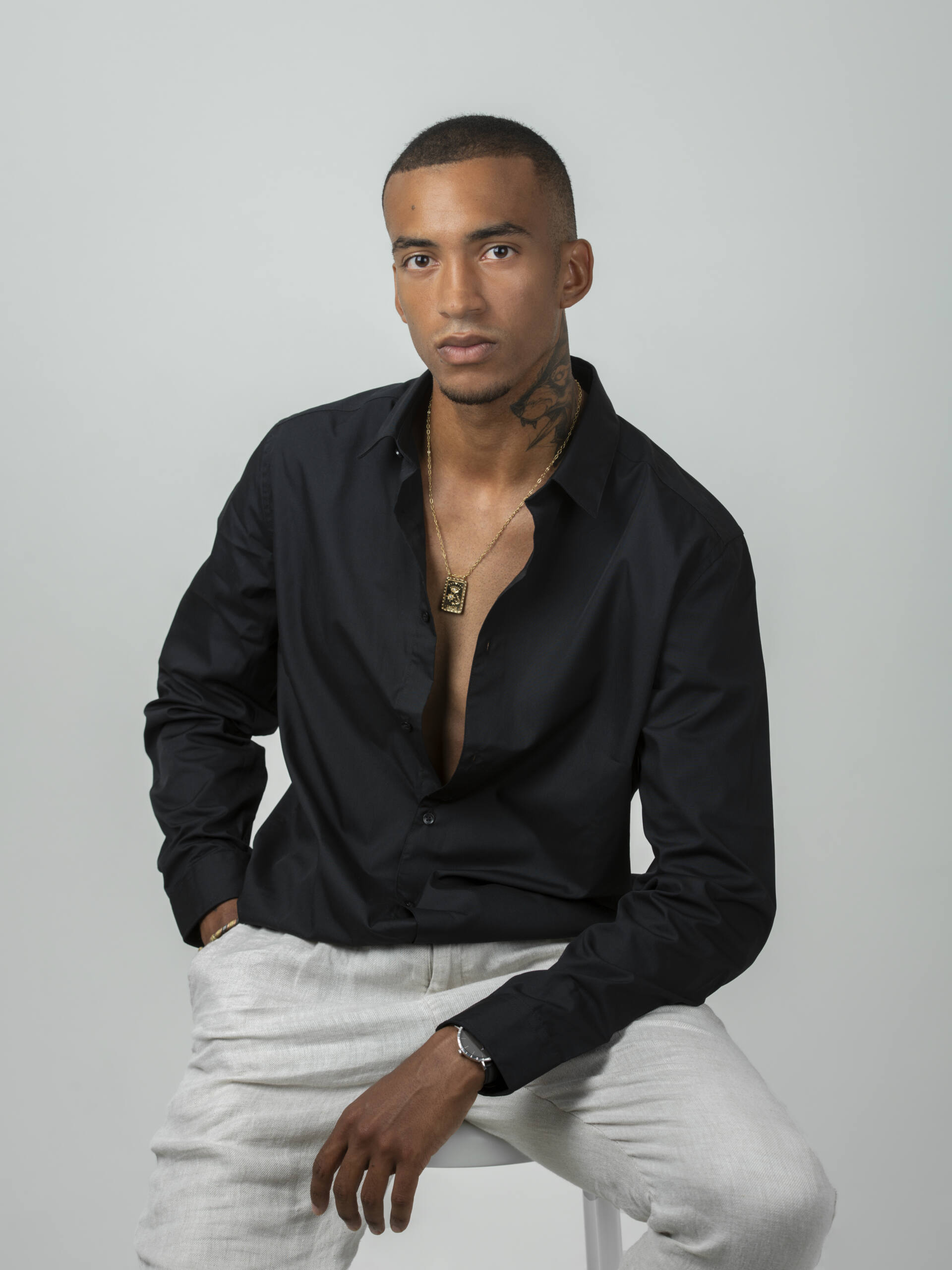 Portrait studio d’un homme en chemise noire, assis sur un tabouret